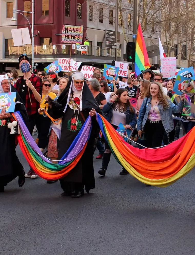 Marchers carrying a long rainbow banner through an Adelaide street.
